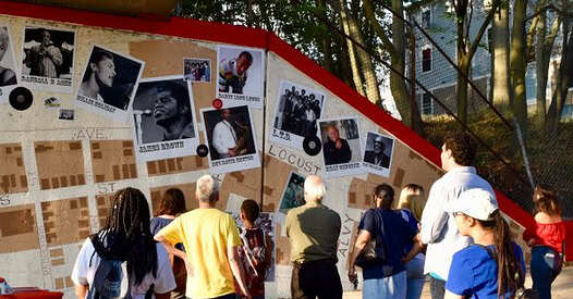 Small crowd viewing the Mt. Hope Music Mural, featuring photos of musicians on a neighborhood map background.