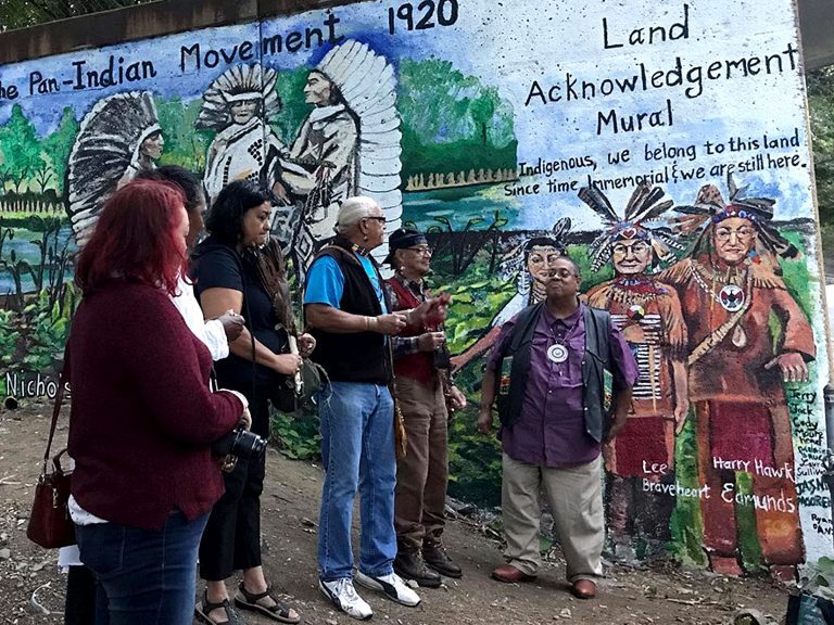 Dedication ceremony for the Land Acknowledgement Mural depicting the Pan-Indian Movement 1920, with community members gathered before it.