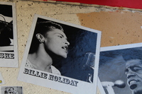 Black-and-white photo of labeled Billie Holiday on textured wall, showing singer mid-performance at a vintage microphone.