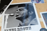 Black-and-white photo of James Brown labeled against a textured wall, singing at a microphone.