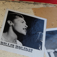 Black-and-white photo of labeled Billie Holiday on textured wall, showing singer mid-performance at a vintage microphone.